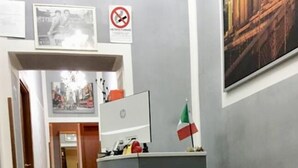 A reception desk with a flag, a bench, and a hallway leading to another room.