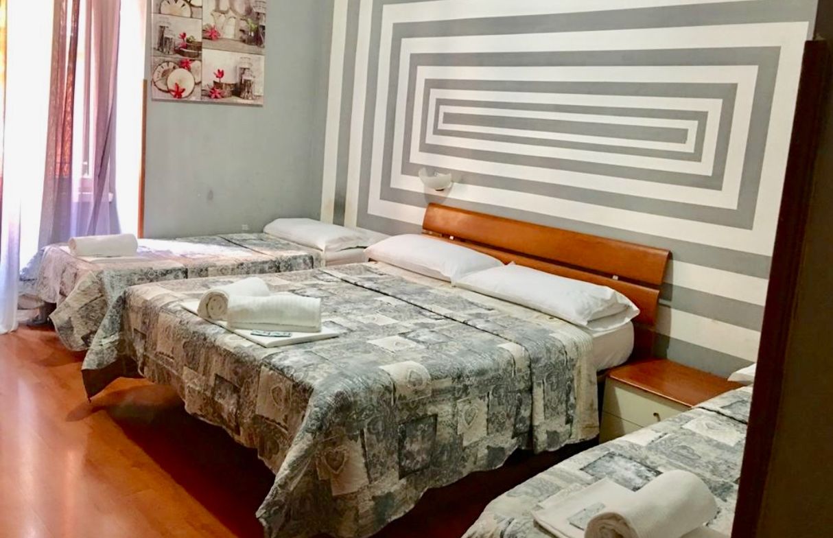 A hotel room with three beds, each with a patterned bedspread and pillows.