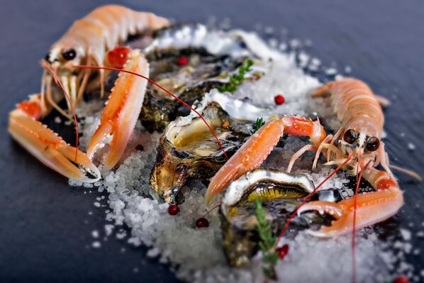 Un plato de mariscos con langosta y ostras sobre una cama de hielo, adornado con hierbas y bayas rojas.
