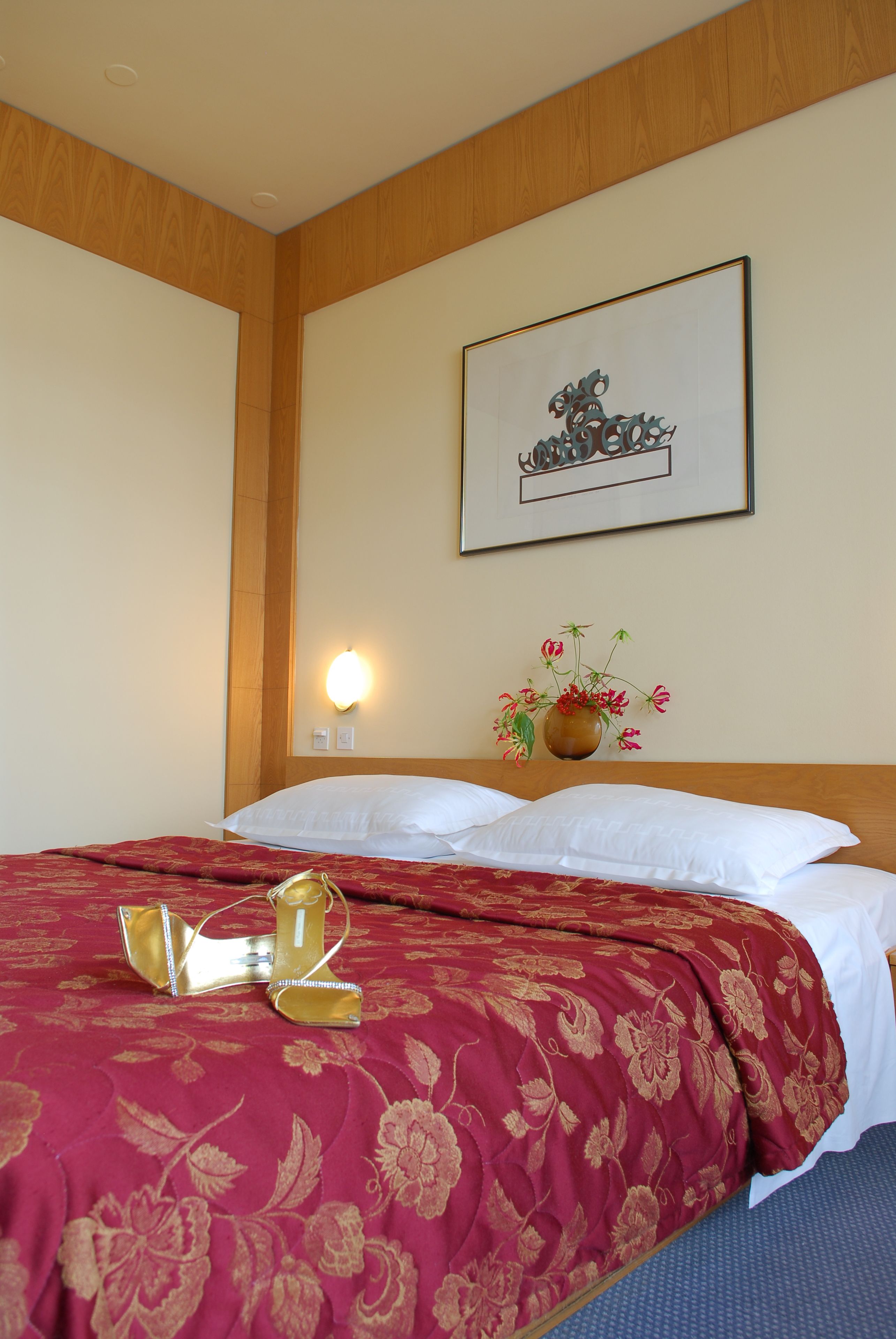 Una habitación de hotel con una cama bien hecha, una obra de arte enmarcada en la pared y un jarrón con flores en la mesita de noche.