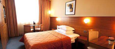 A hotel room with a bed, a desk, a chair, a small table, and a picture on the wall.