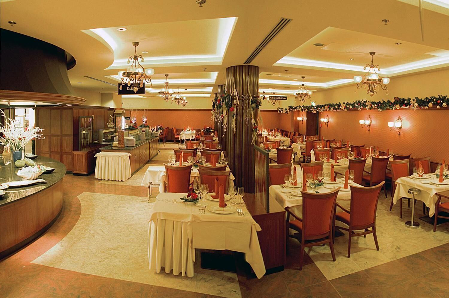 Un restaurant doté de nombreuses tables, de lustres et d’une colonne décorative centrale.