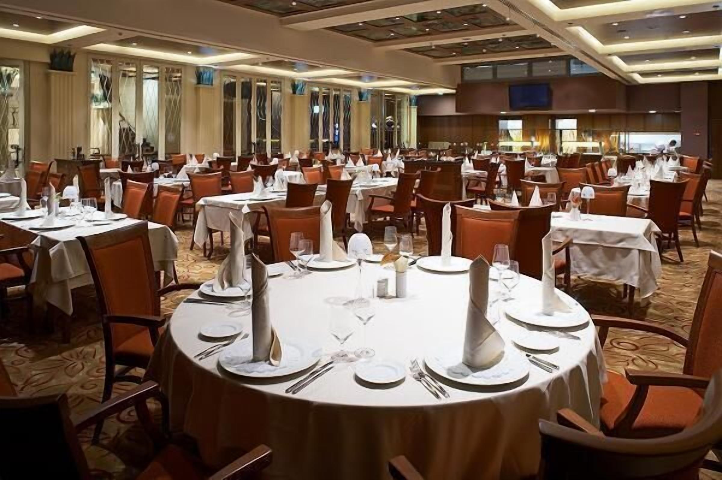 A large banquet hall with round tables set for dining, featuring white tablecloths and silverware.
