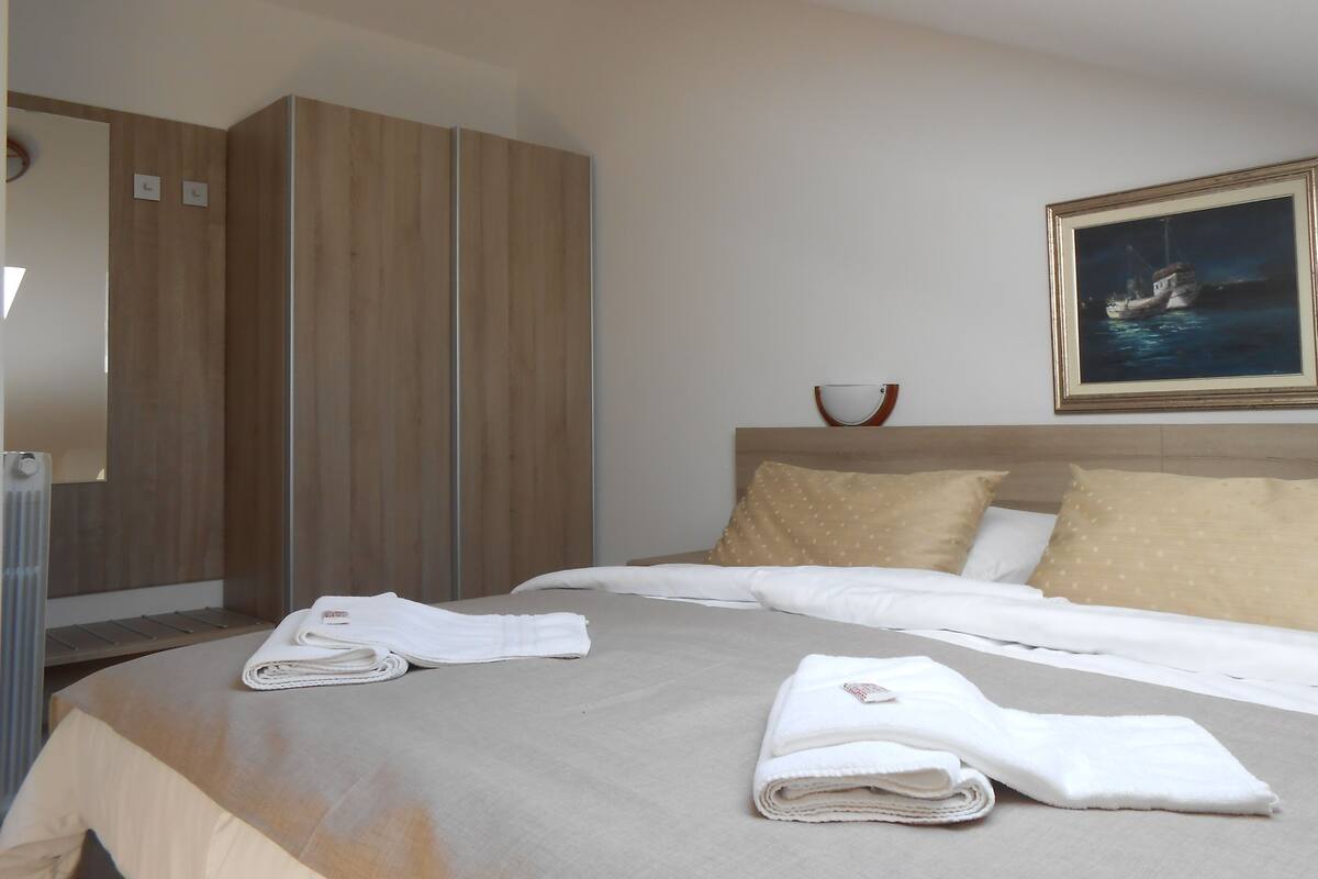 A neatly made bed with white linens, a wooden wardrobe, and a framed picture of a boat on the wall.