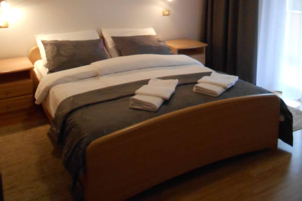 A neatly made bed with a wooden headboard, two bedside tables with lamps, a framed picture on the wall, and a window with curtains.