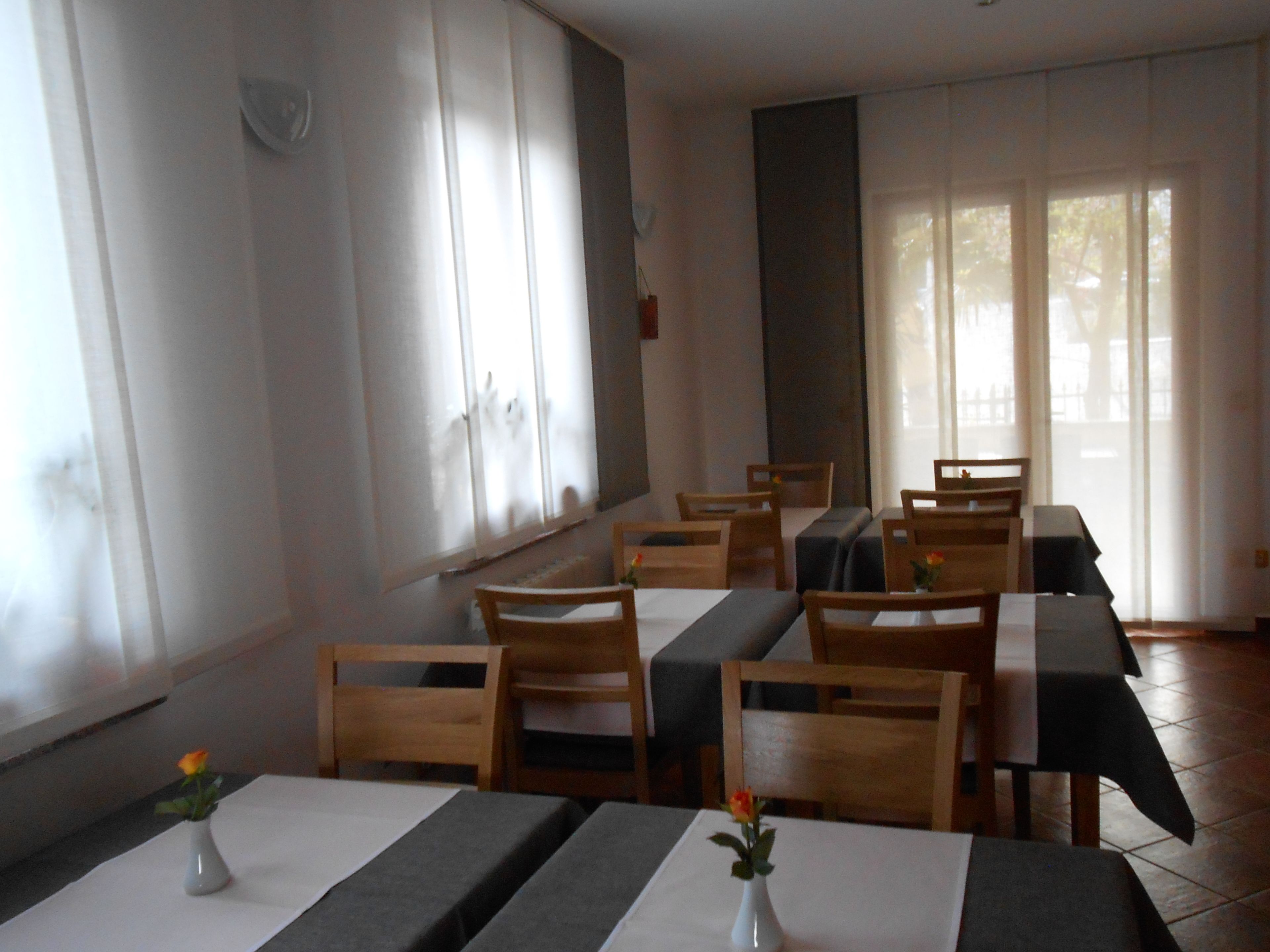 A dining area with tables and chairs, large windows, and a view of the outside.