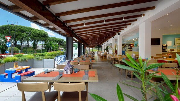 An outdoor café with wooden tables and chairs, surrounded by greenery and a clear view of the sky.