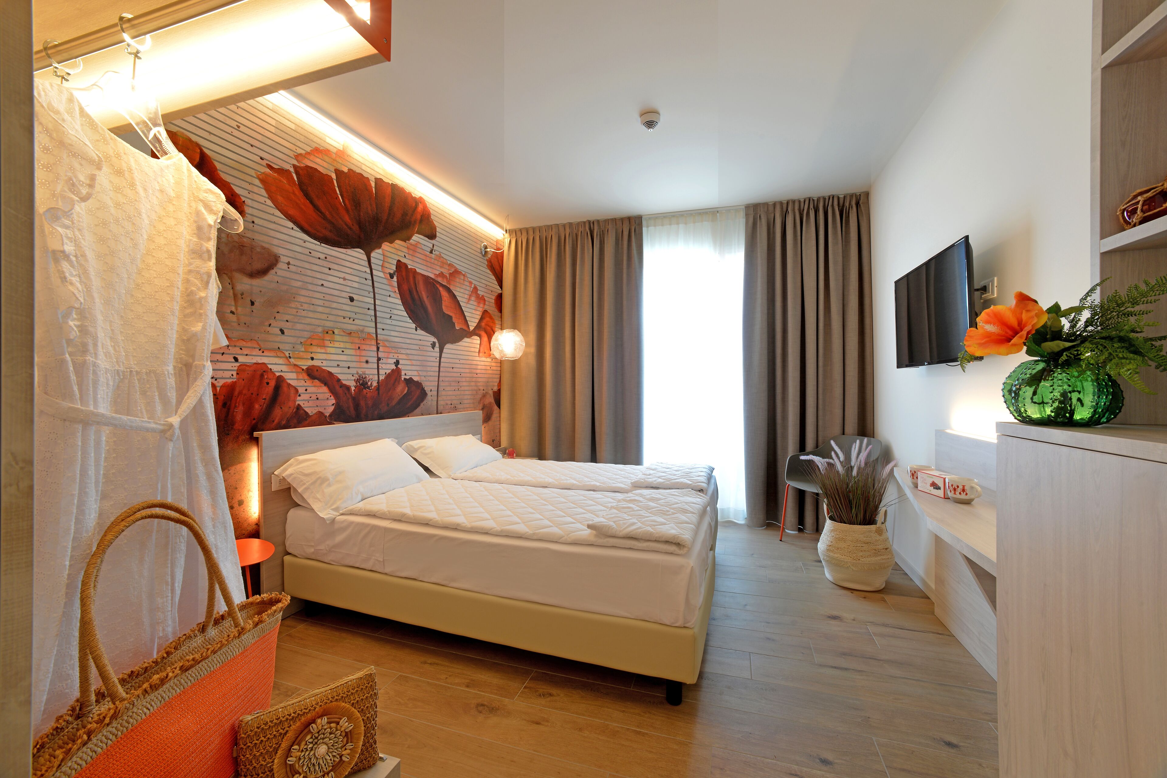 Quarto com cama, um mural grande na parede, televisão e um vaso de planta.