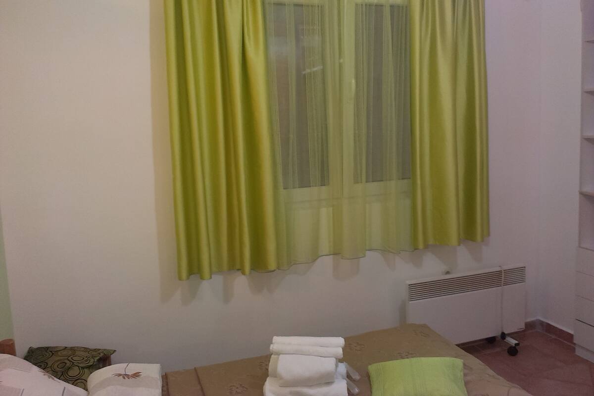 A room with a bed, a radiator, and a window with green curtains.