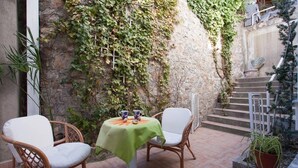 A patio with wicker chairs and a table, a stone wall with ivy, and a staircase. - Apartments Kosta (Ohrid)