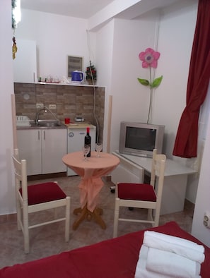 A compact room with a kitchenette, a small dining table with two chairs, a TV, and a bed with a red blanket. - Apartments Kosta (Ohrid)