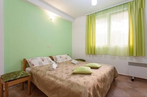 A bedroom with a bed, pillows, a nightstand, and a window with curtains. - Apartments Kosta (Ohrid)