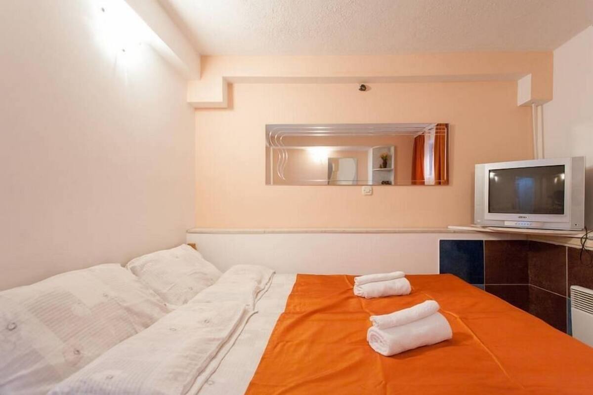 A hotel room with a bed, an orange blanket, a television, and a mirror.