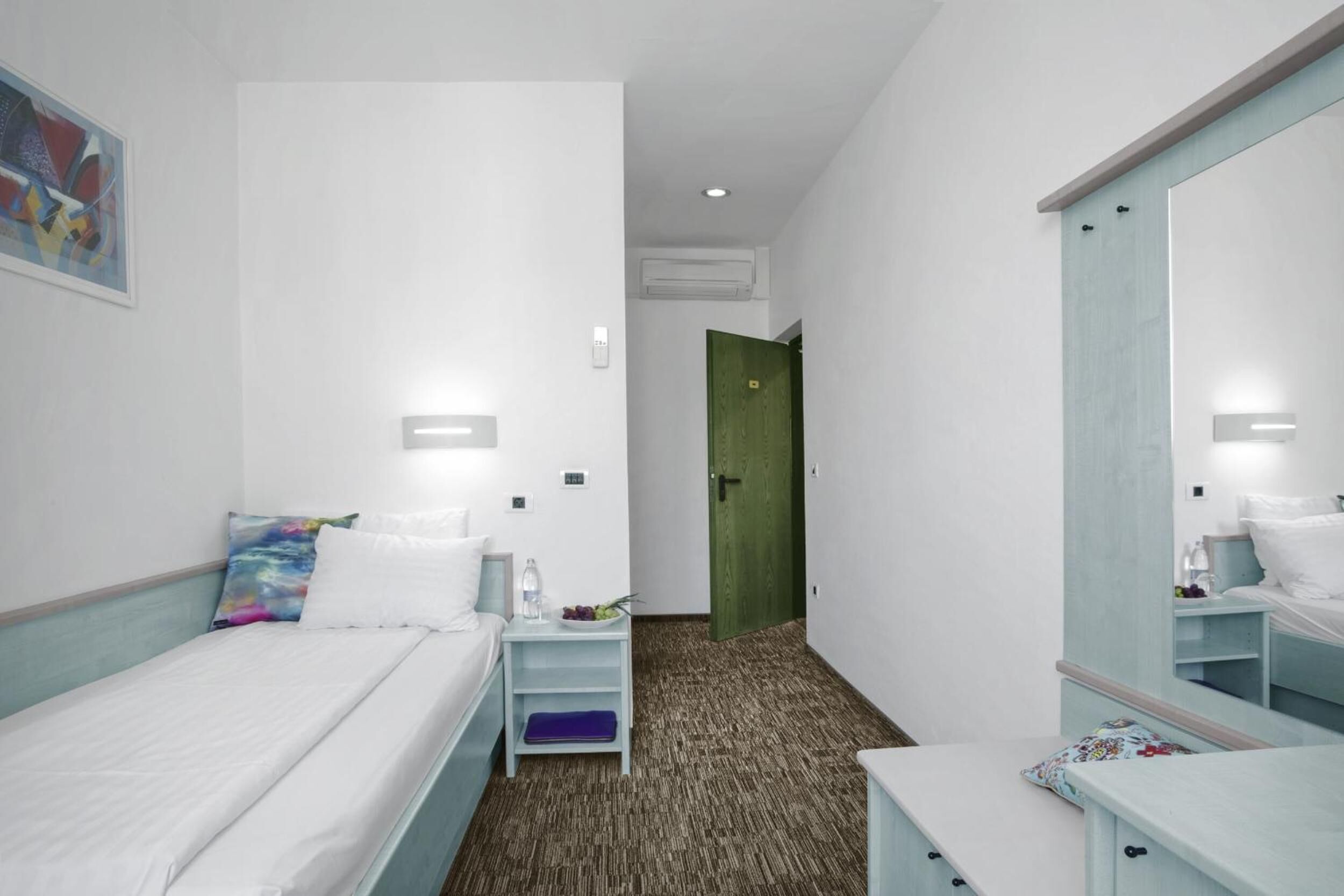Una habitación de hotel con cama, mesita de noche, cómoda, espejo y puerta.