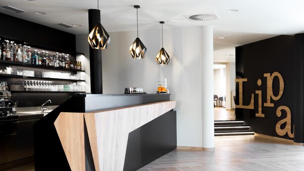 Zona de bar moderna con mostrador de madera, lámparas colgantes y una barra repleta de botellas y copas.