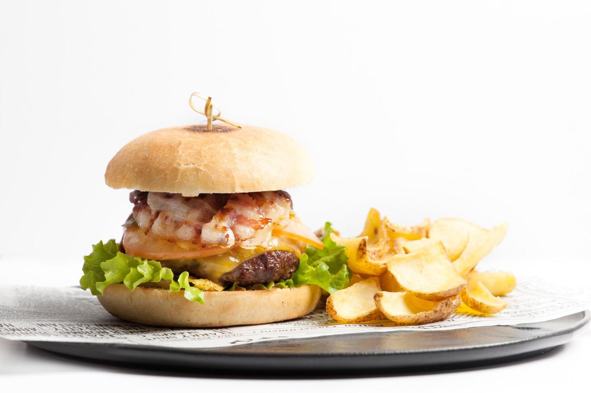 A burger with bacon, lettuce, and a bun, accompanied by potato chips on a plate.
