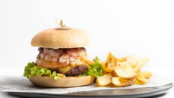 A burger with bacon, lettuce, and a bun, accompanied by potato chips on a plate.