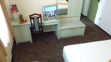 Habitación de hotel compacta con cama, un escritorio pequeño con televisor, una silla y una mesita con frutas.