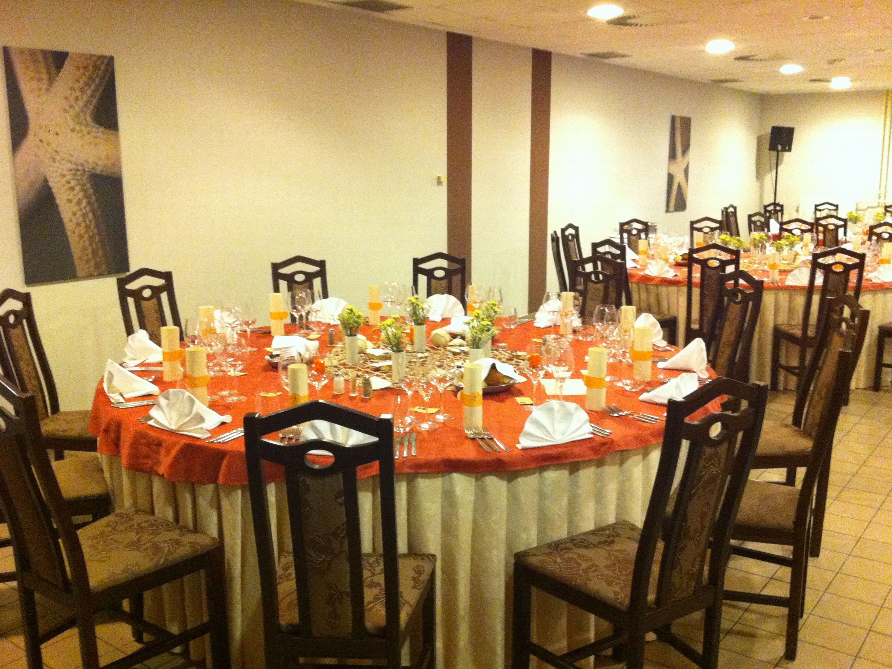 Un comedor con mesas redondas dispuestas para varios comensales, cada una con sillas y cubiertos, platos y cristalería.