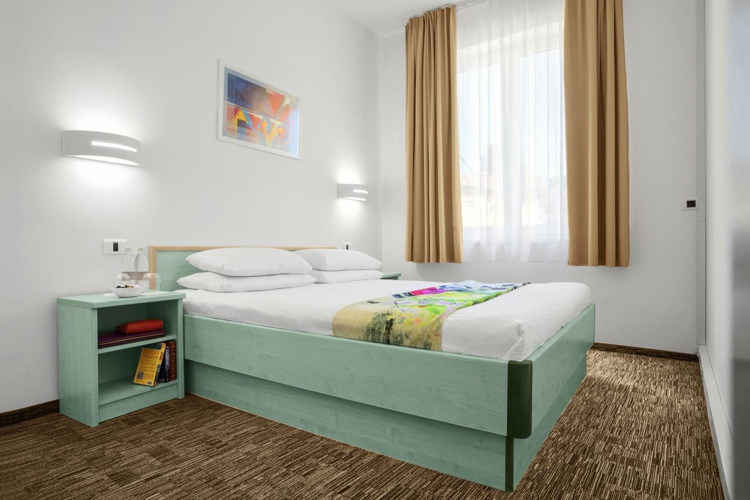 Una habitación de hotel con cama, mesita de noche, estantería y ventana con cortinas.