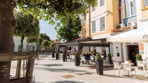 Un área de café al aire libre con mesas y sillas, rodeada de edificios con señalización para un hotel y un bar.