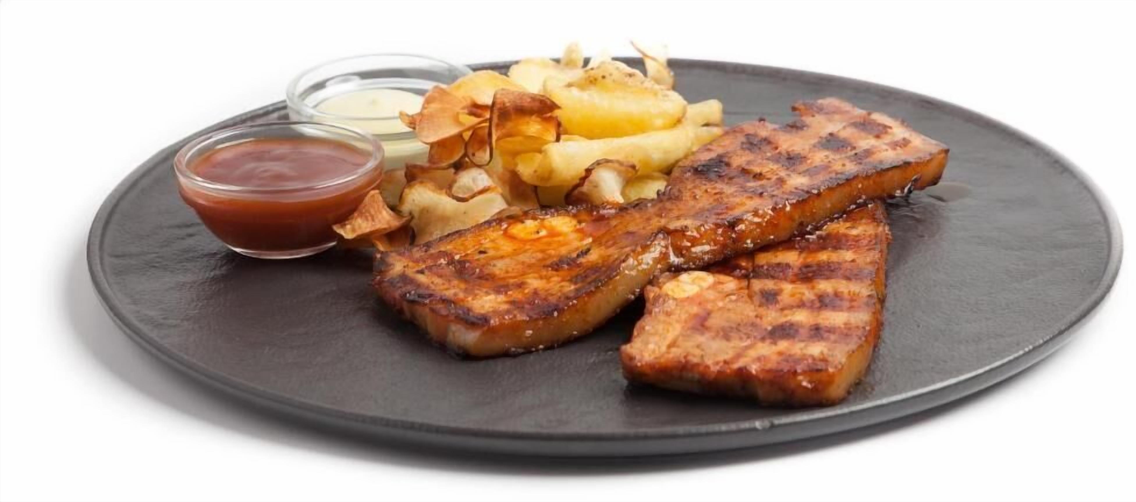 Un piatto con bistecca alla griglia, patatine fritte e una piccola ciotola di ketchup.