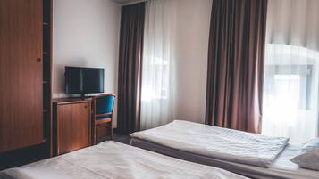 A hotel room with two single beds, a wooden wardrobe, a desk with a television, and curtains.