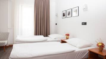 A hotel room with two single beds, a chair, a nightstand with a vase of flowers, and a window with curtains.