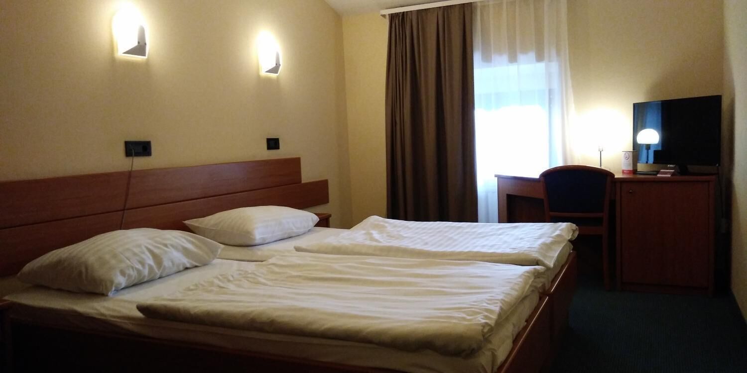 A hotel room with two beds, a desk, a chair, and a television.