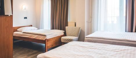 Habitación de hotel con dos camas, una silla, un radiador y una ventana con cortinas.