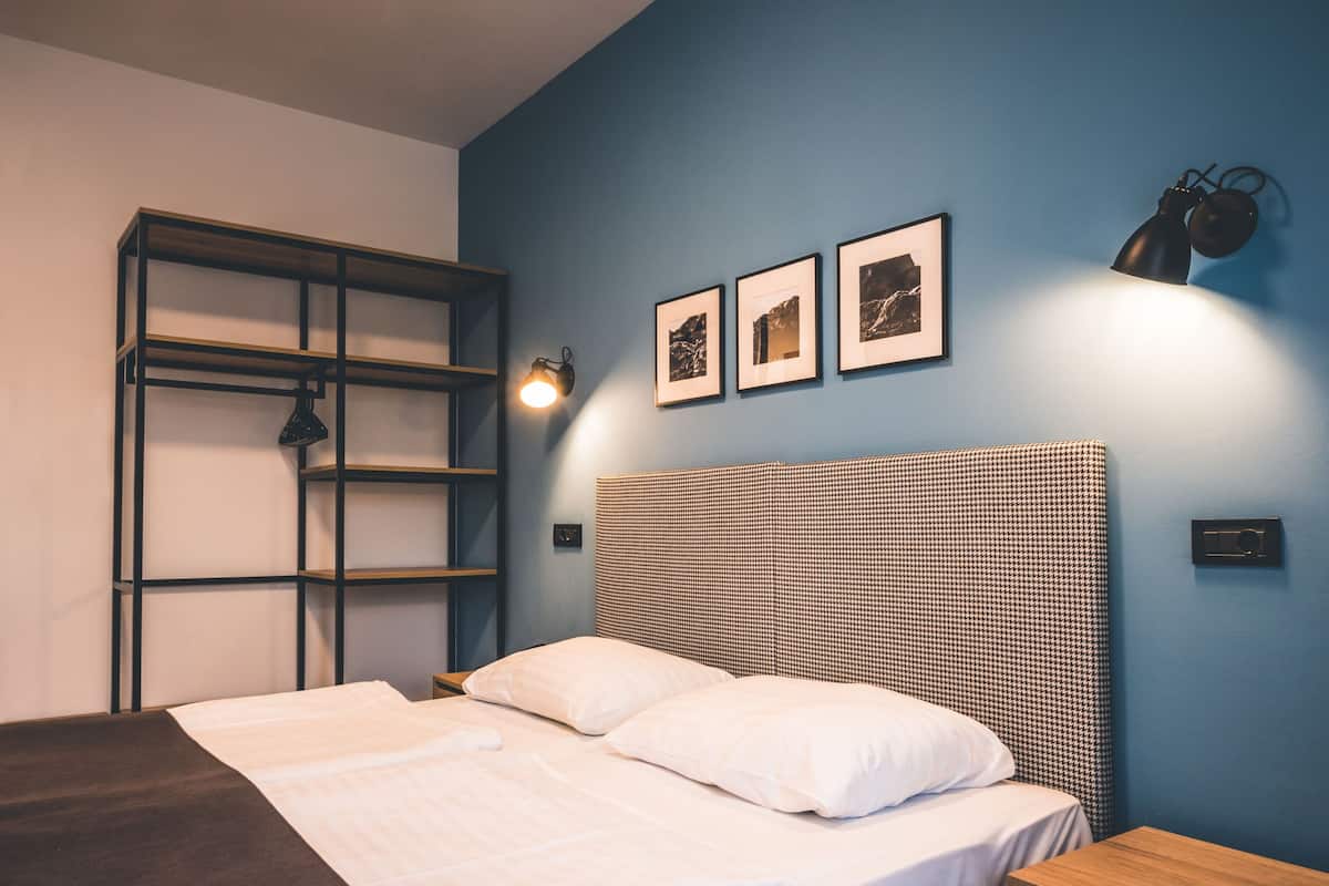 Ein ordentlich bezogenes Bett mit weißen Leinentüchern, einem Kopfende mit Hounds-Tooth-Muster und einem Nachttisch aus Holz mit einer Schublade.