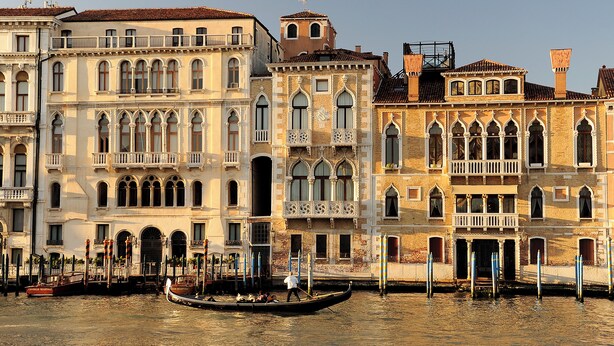 Un canal bordé de gondoles et de bâtiments historiques dotés de balcons et de fenêtres en arc de cercle.