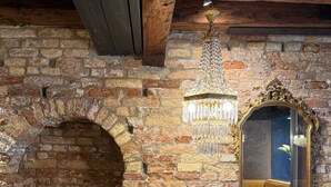 Un mur en pierre rustique, un plafond avec une poutre en bois, un lustre et un miroir qui reflète une pièce avec un canapé.