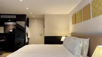 Quarto de hotel com cama, luminárias de cabeceira, uma escrivaninha e um guarda-roupa.