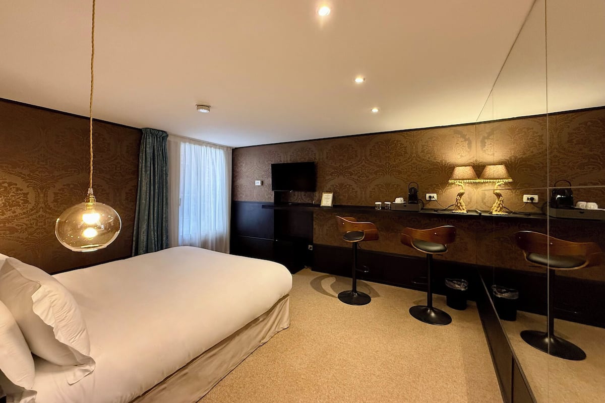 A modern hotel room with a large bed, a vanity with a mirror, and a bar area with stools.