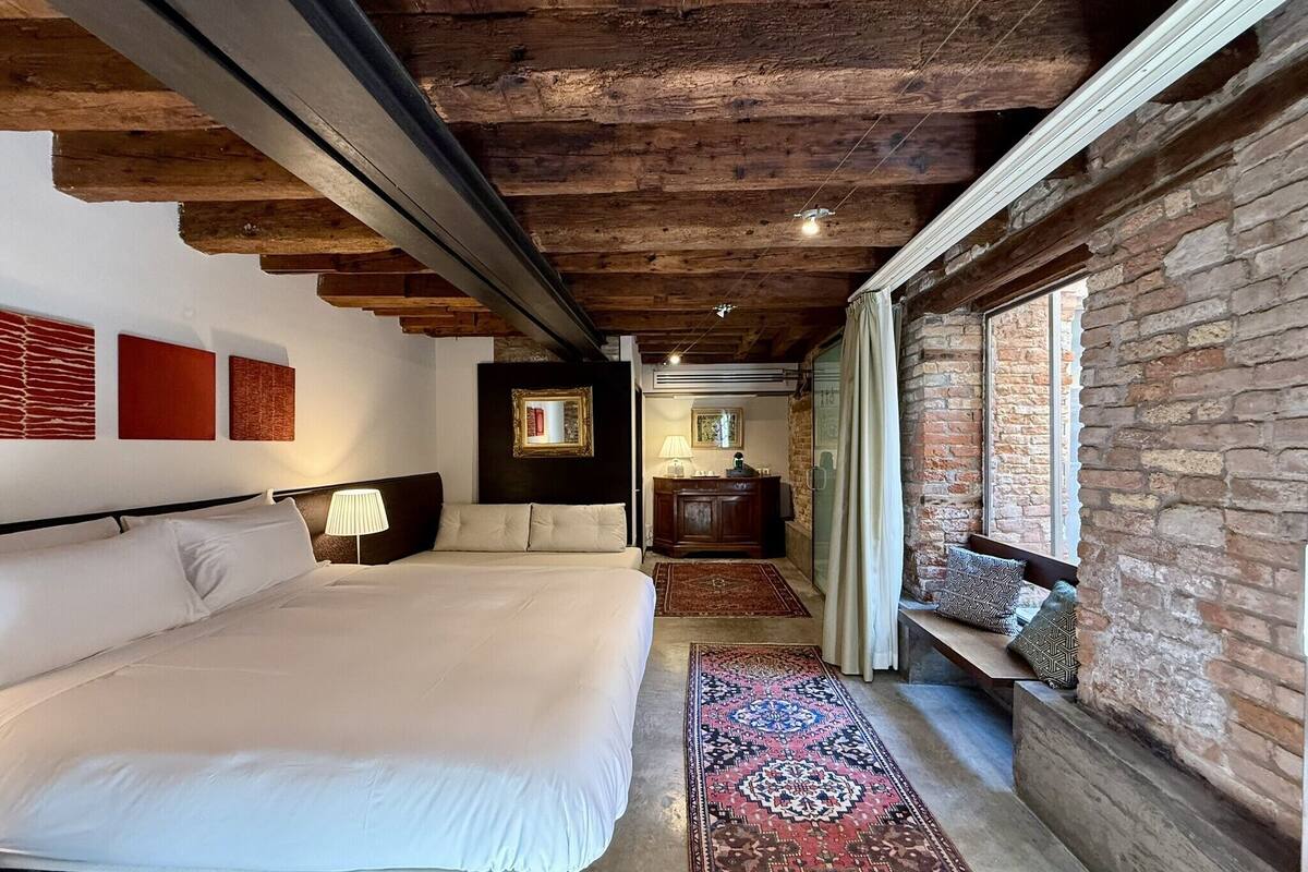 A bedroom with a large bed, a wooden ceiling, a brick wall, and a window.