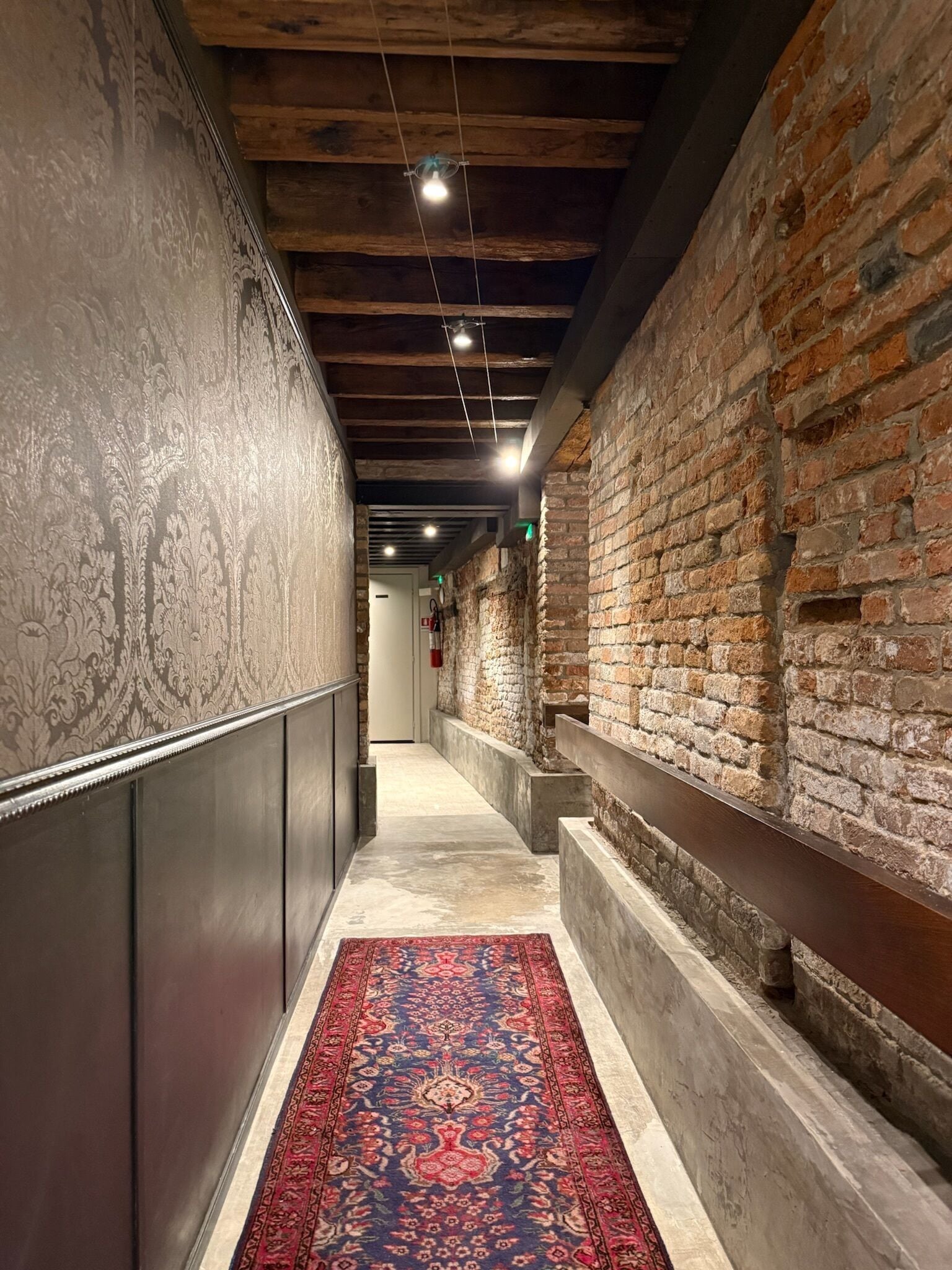 Un couloir avec un mur orné de motifs, un mur en briques et une moquette rouge.