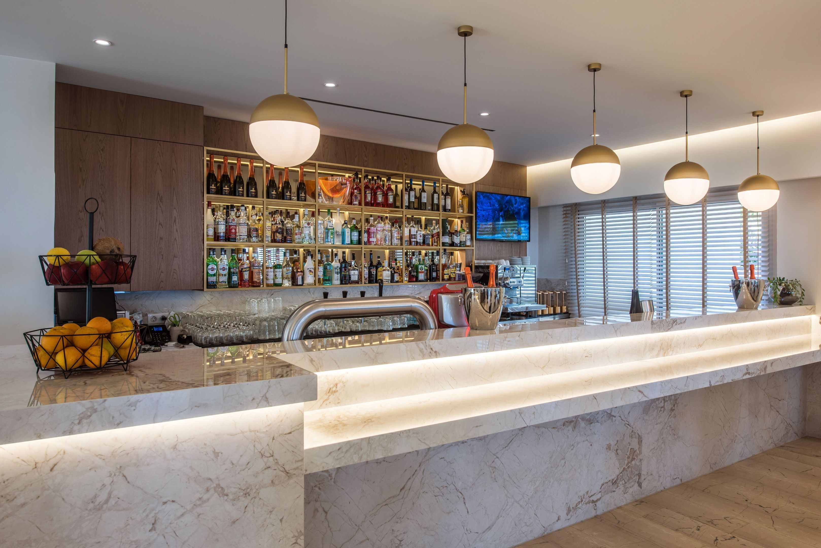 Eine moderne Bar mit einer Marmor-Arbeitsplatte, Pendelleuchten an der Decke und einem Weinkühlschrank, gefüllt mit Flaschen.