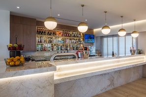 A modern bar area with a marble countertop, overhead pendant lighting, and a wine rack filled with bottles.