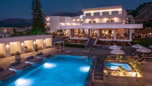 Een modern hotel met een zwembadgedeelte, terras en een berg op de achtergrond.