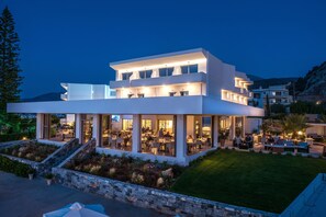 A modern multi-story building with a dining area and outdoor seating. - Hotel Matheo Villas & Suites (Hersonissos)