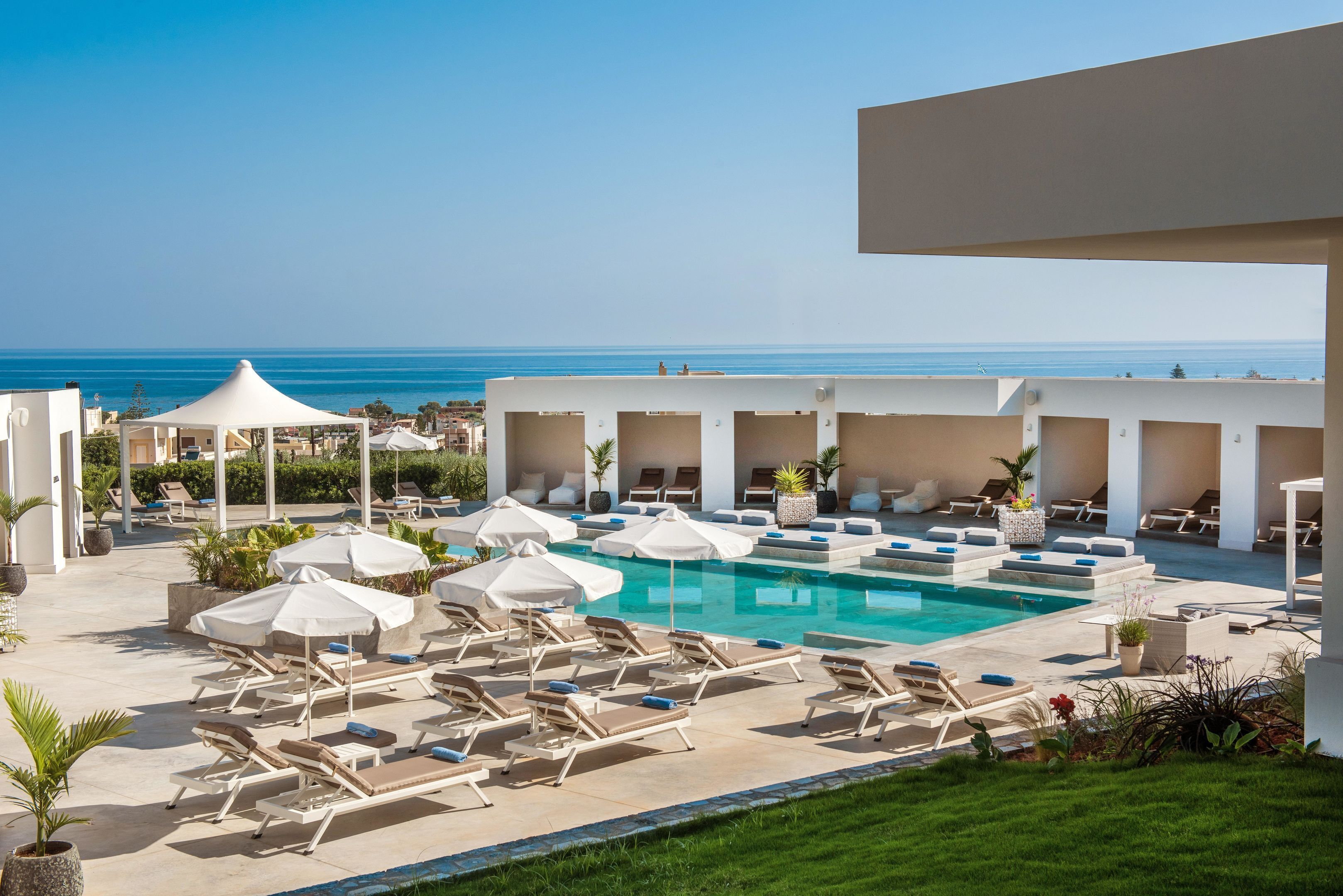 A poolside area with lounge chairs and umbrellas, overlooking a clear blue sea.