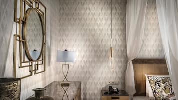 Una habitación de hotel con cama, mesita de noche, lámpara, teléfono y un espejo decorativo.