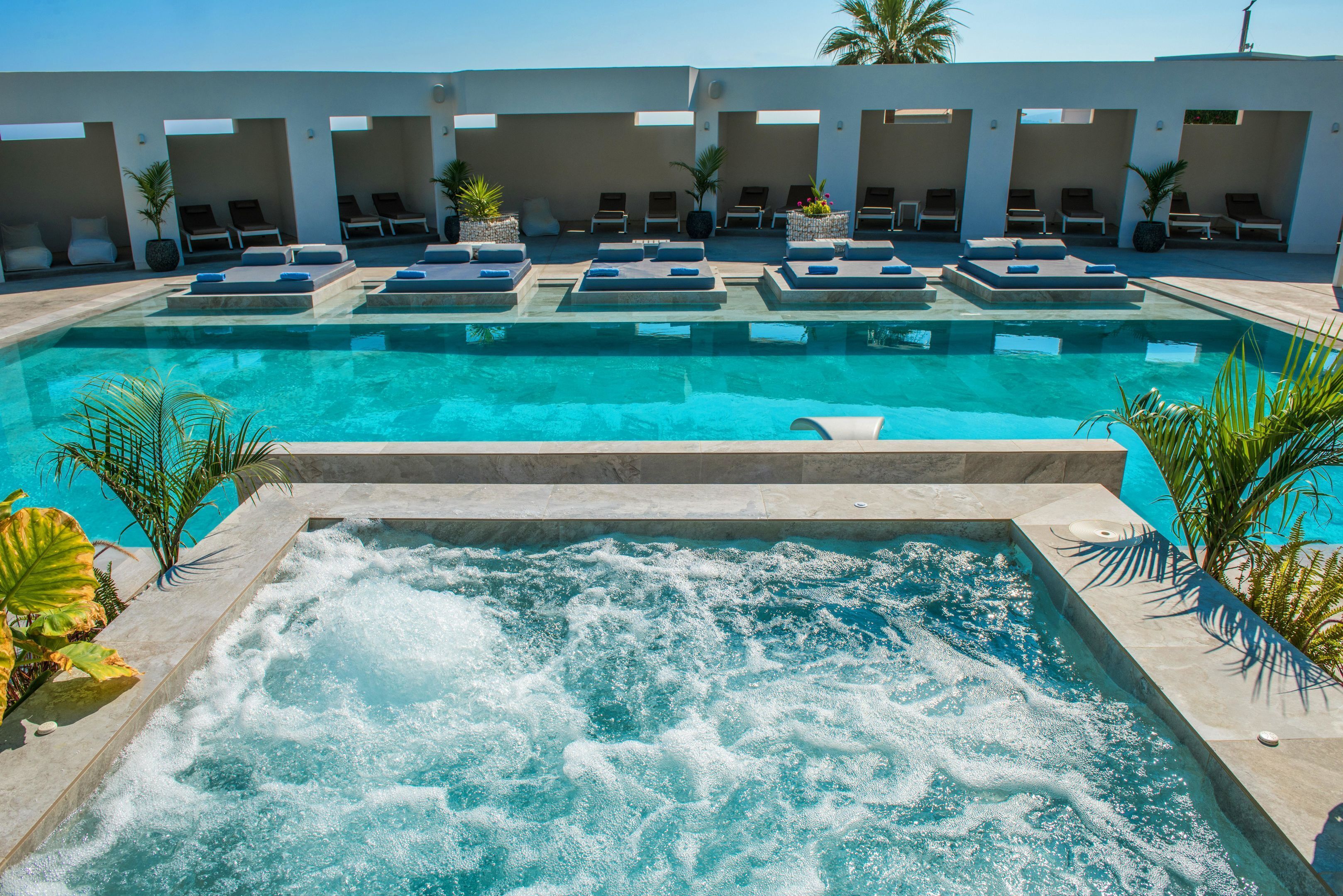 Ein Swimmingpool mit Whirlpool, Liegestühlen und Palmen.