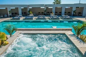A swimming pool with a hot tub area, lounge chairs, and palm trees. - Hotel Matheo Villas & Suites (Hersonissos)