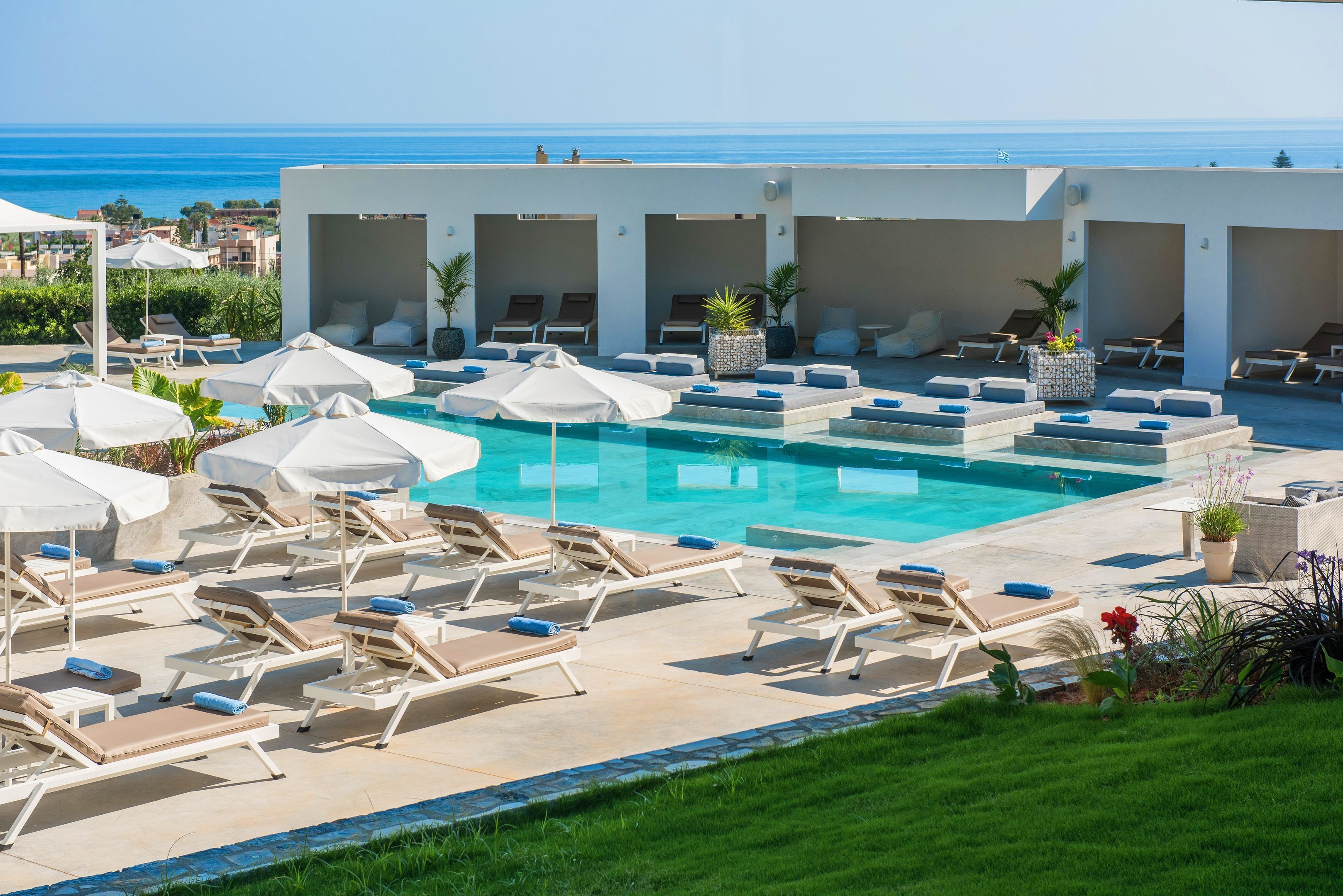 A poolside area with lounge chairs and umbrellas, a clear view of the ocean, and a well-maintained lawn.