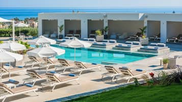 A poolside area with lounge chairs and umbrellas, a clear view of the ocean, and a well-maintained lawn.