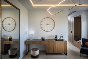 A modern hotel lobby with two large wall clocks, a wooden console table with a coffee machine, and a seating area with a chair.
