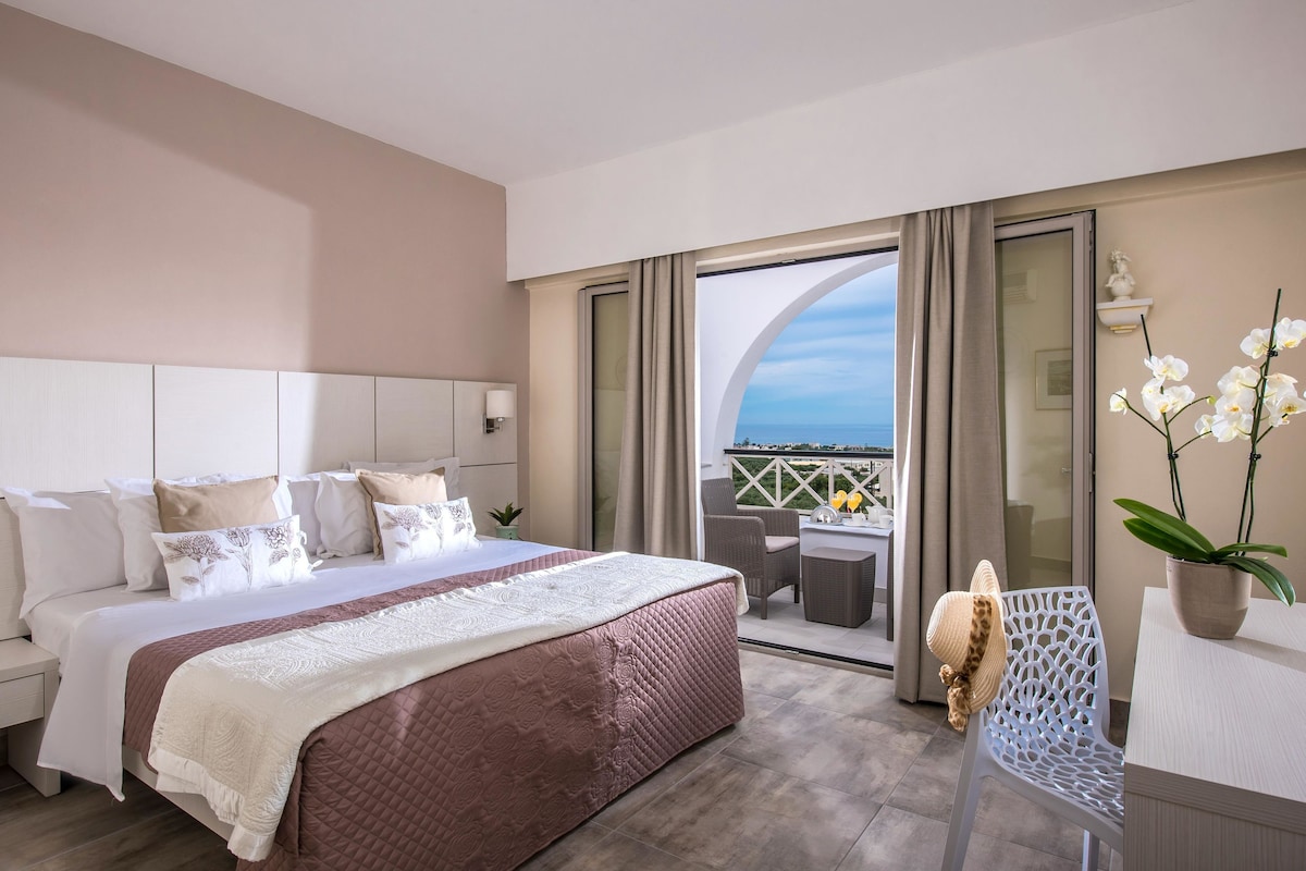 Ein Hotelzimmer mit einem großen Bett, einem Balkon mit Blick und einem Essbereich.