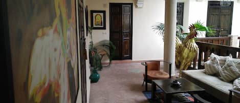 A room with a herringbone floor, a sofa, a table, and a chair. There is a door with a decorative frame and a plant near it.